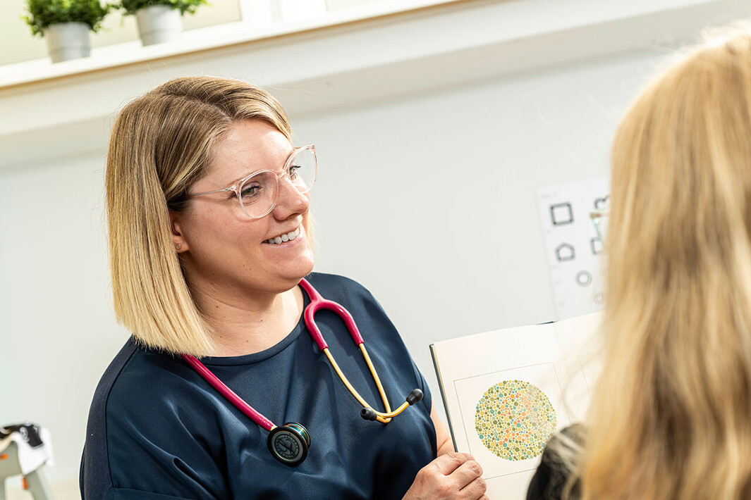 Frau führt mit einem Kind einen Hör- und Sehtest durch, beide sitzen sich gegenüber.